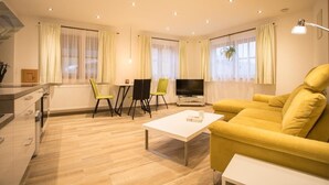 Una sala de estar moderna con un sofá amarillo, una mesa de centro blanca, un televisor y un comedor con sillas.