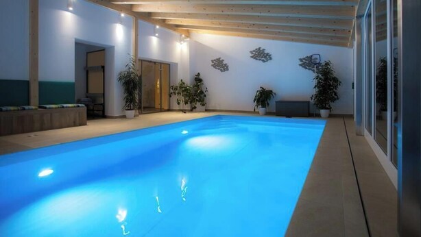 Una piscina interior con vigas de madera, plantas en macetas y una banca.