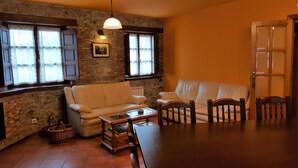 A cozy living room with a stone wall, a wooden floor, a white sofa, a wooden coffee table, and a wicker basket.