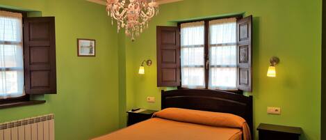 Un dormitorio con paredes verdes, una cama de madera, un candelabro y dos ventanas con cortinas.