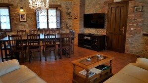 A cozy living room with a fireplace, a dining area with wooden chairs, a television, and a sofa.