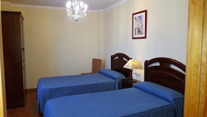 A room with two beds, a chandelier, a framed picture on the wall, and a wooden wardrobe.