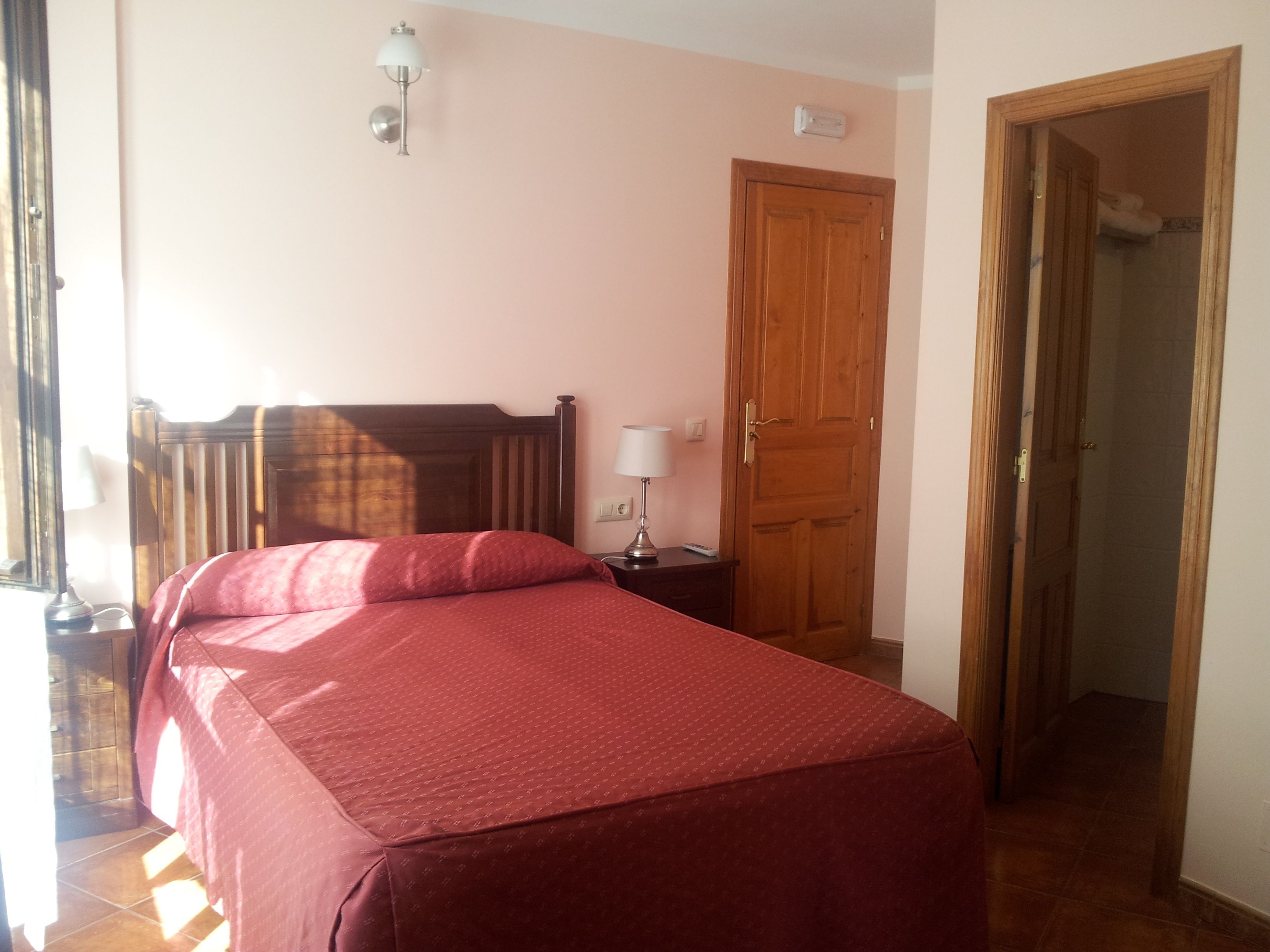 A bedroom with a bed, a nightstand, a lamp, a wooden door, and a light switch on the wall.