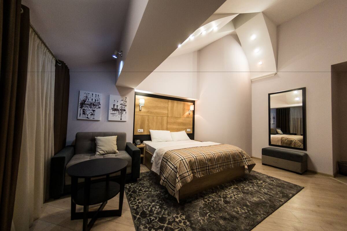 A modern hotel room with a bed, a sofa, a small table, and a mirror.