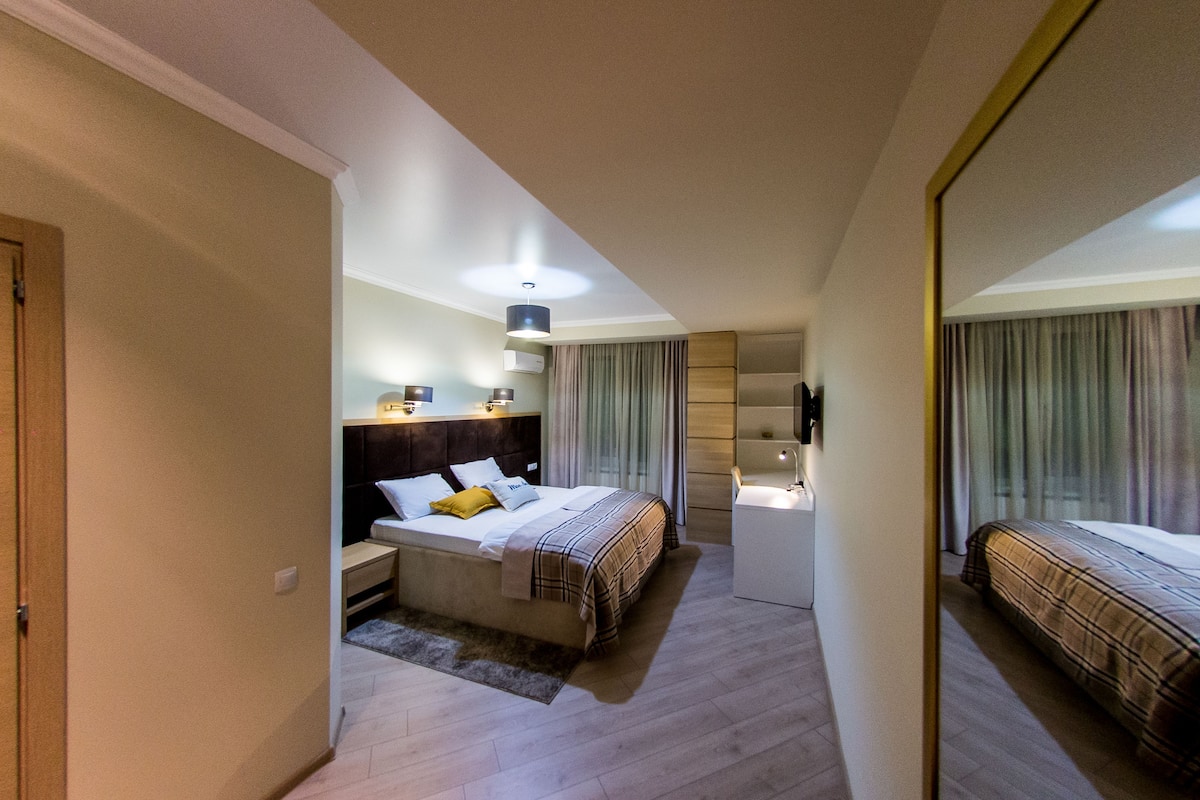 A modern hotel room with a large bed, bedside tables, a desk, and a mirror.