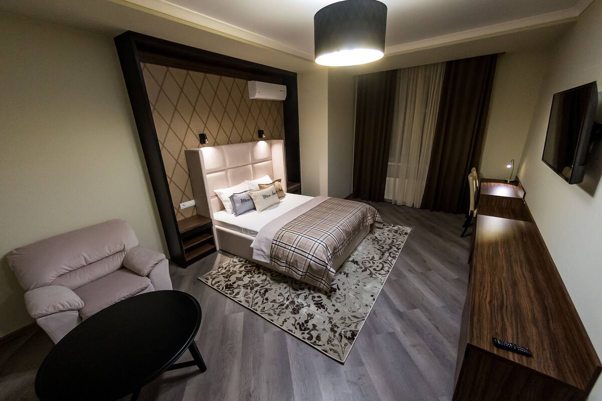 A modern hotel room with a large bed, a sofa, a desk, and a TV.