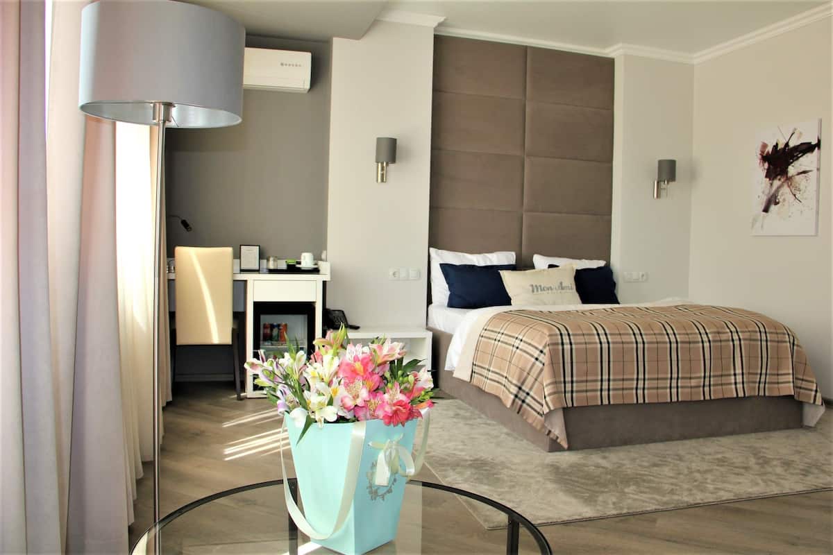 A modern hotel room with a large bed, a desk, and a glass table with a bouquet of flowers.