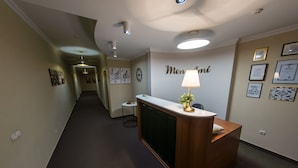 A reception area with a wooden reception desk, a wall-mounted lamp, framed certificates, and a hallway leading to another room. - Mon Ami Villa (Chisinau)