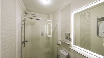 A bathroom with white tiled walls, a glass shower enclosure, a toilet, and a mirror.