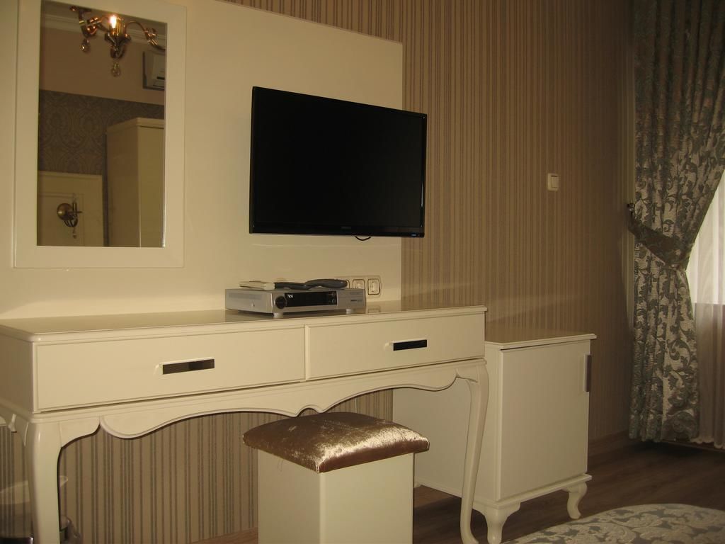 A white vanity with a flat-screen TV mounted above it, a mirror, and a small drawer unit.