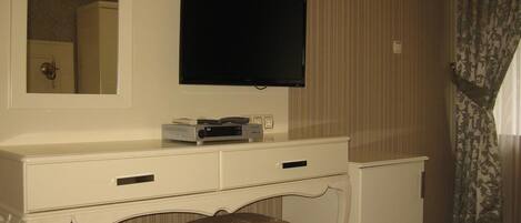 A white vanity with a flat-screen TV mounted above it, a mirror, and a small drawer unit.