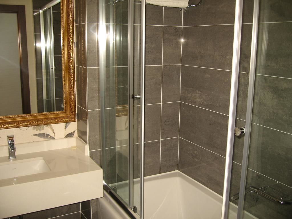 A modern bathroom with a glass shower enclosure, a white sink, and a large mirror with a gold frame.
