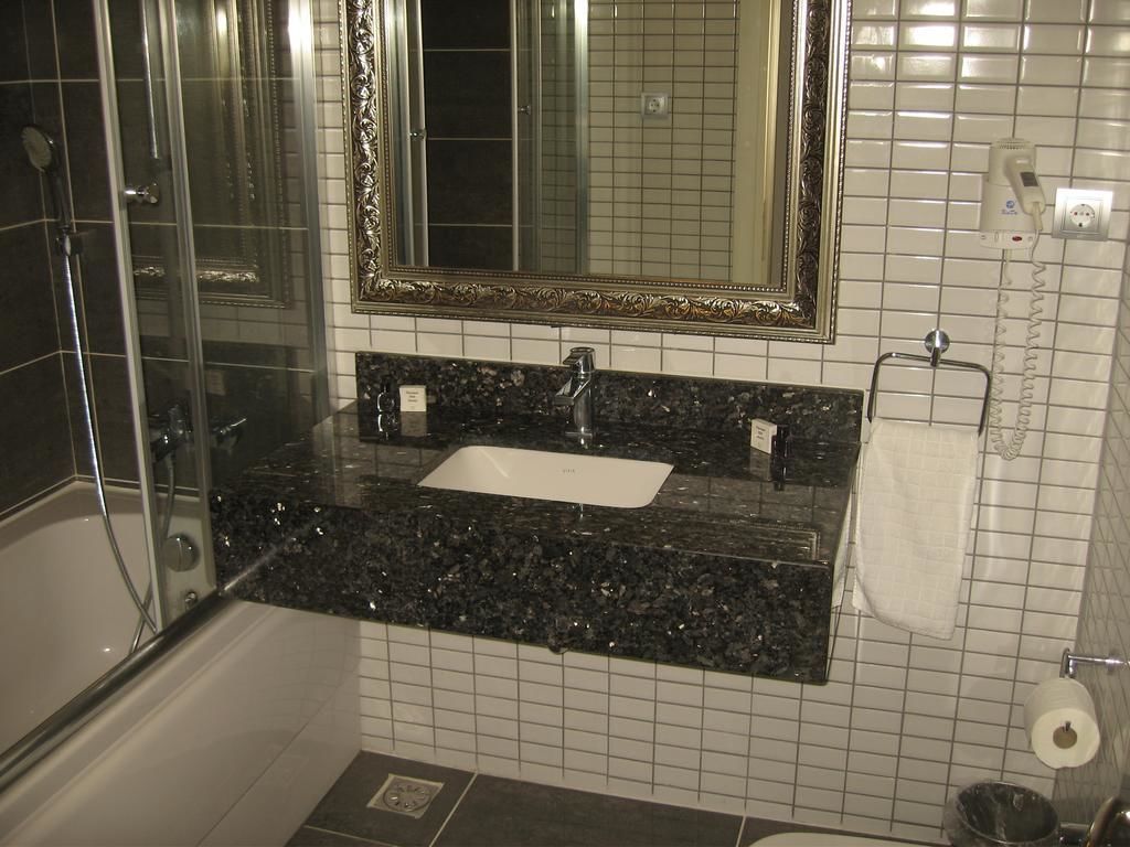 A bathroom with a glass shower enclosure, a sink with a marble countertop, a large mirror with an ornate frame, and a towel rack.