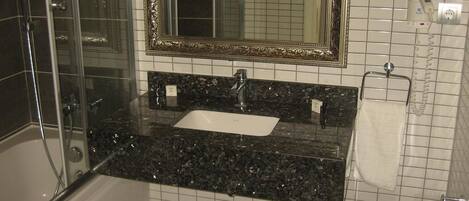 A bathroom with a glass shower enclosure, a sink with a marble countertop, a large mirror with an ornate frame, and a towel rack.