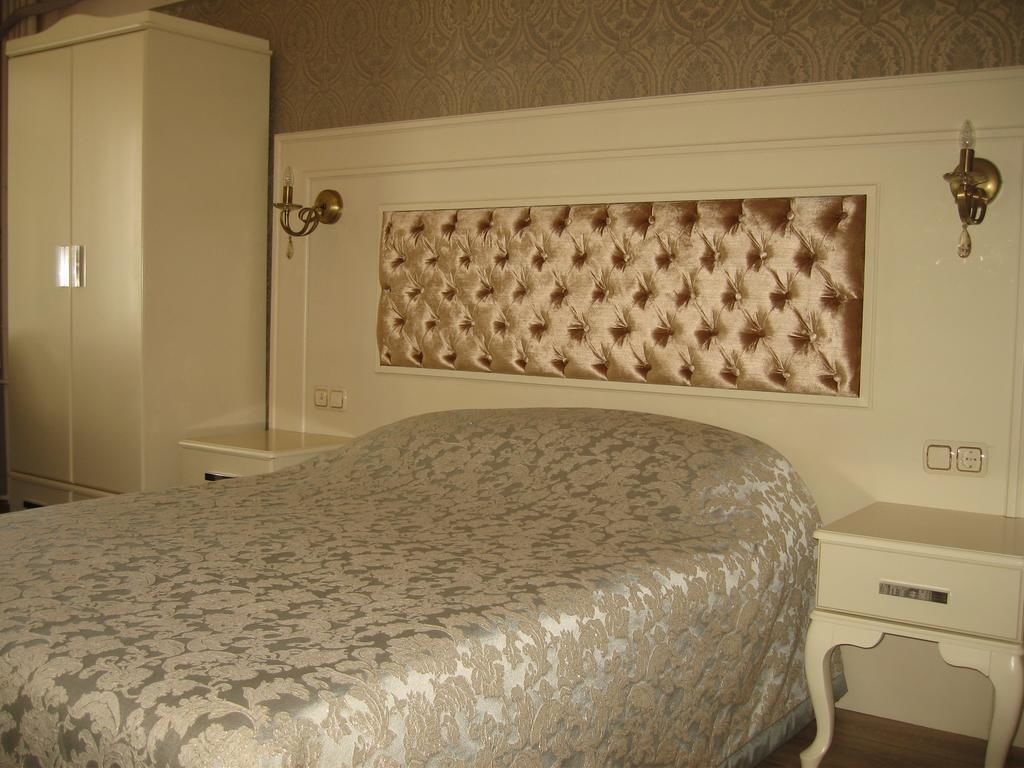 Un dormitorio con tablero de cama capitonado, colcha estampada, mesita de noche y armario.