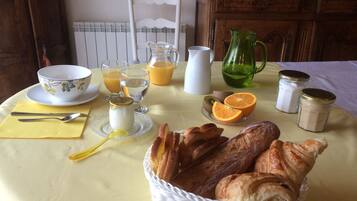 Une table de petit-déjeuner avec du pain, des viennoiseries, des fruits et des boissons.