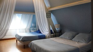 Quarto com duas camas, janela com cortinas leves, mesa de cabeceira com abajur e um quadro na parede.