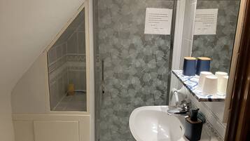 Une salle de bain avec une douche, un lavabo et un miroir. On y trouve des serviettes et un distributeur de savon sur le lavabo.