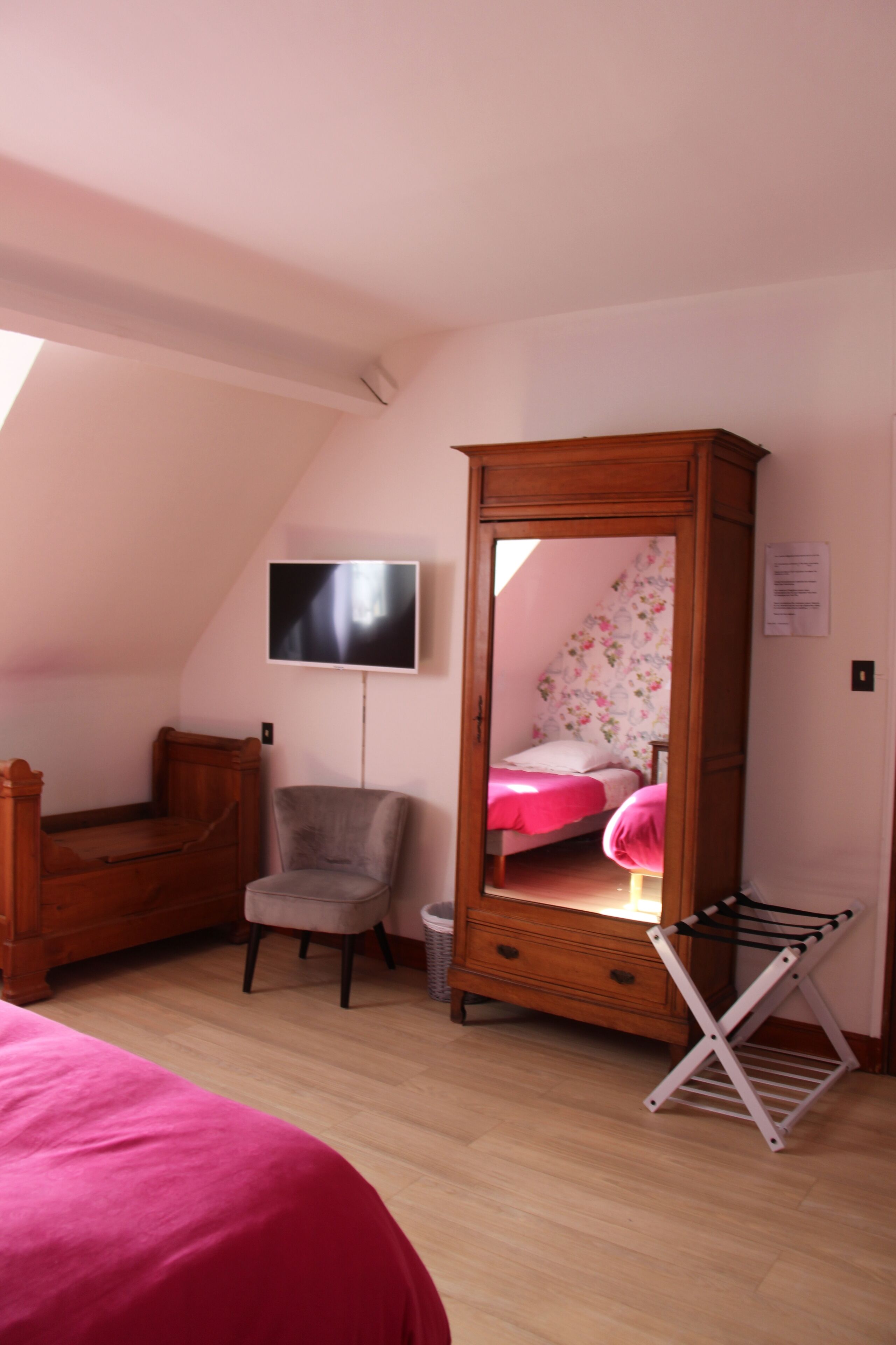 Une chambre avec une armoire en bois, une chaise, un lit, un téléviseur et un miroir.