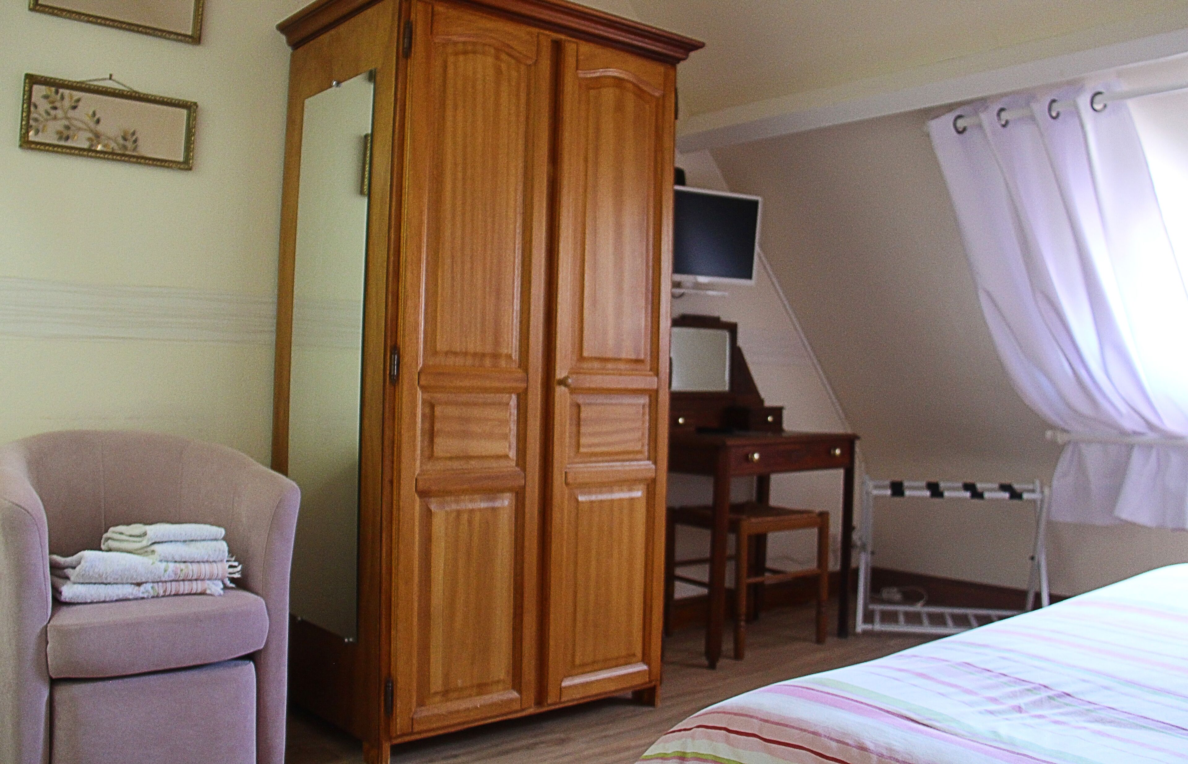 Une chambre à coucher avec une armoire en bois, un bureau avec un ordinateur, une chaise, un lit et une fenêtre avec des rideaux.