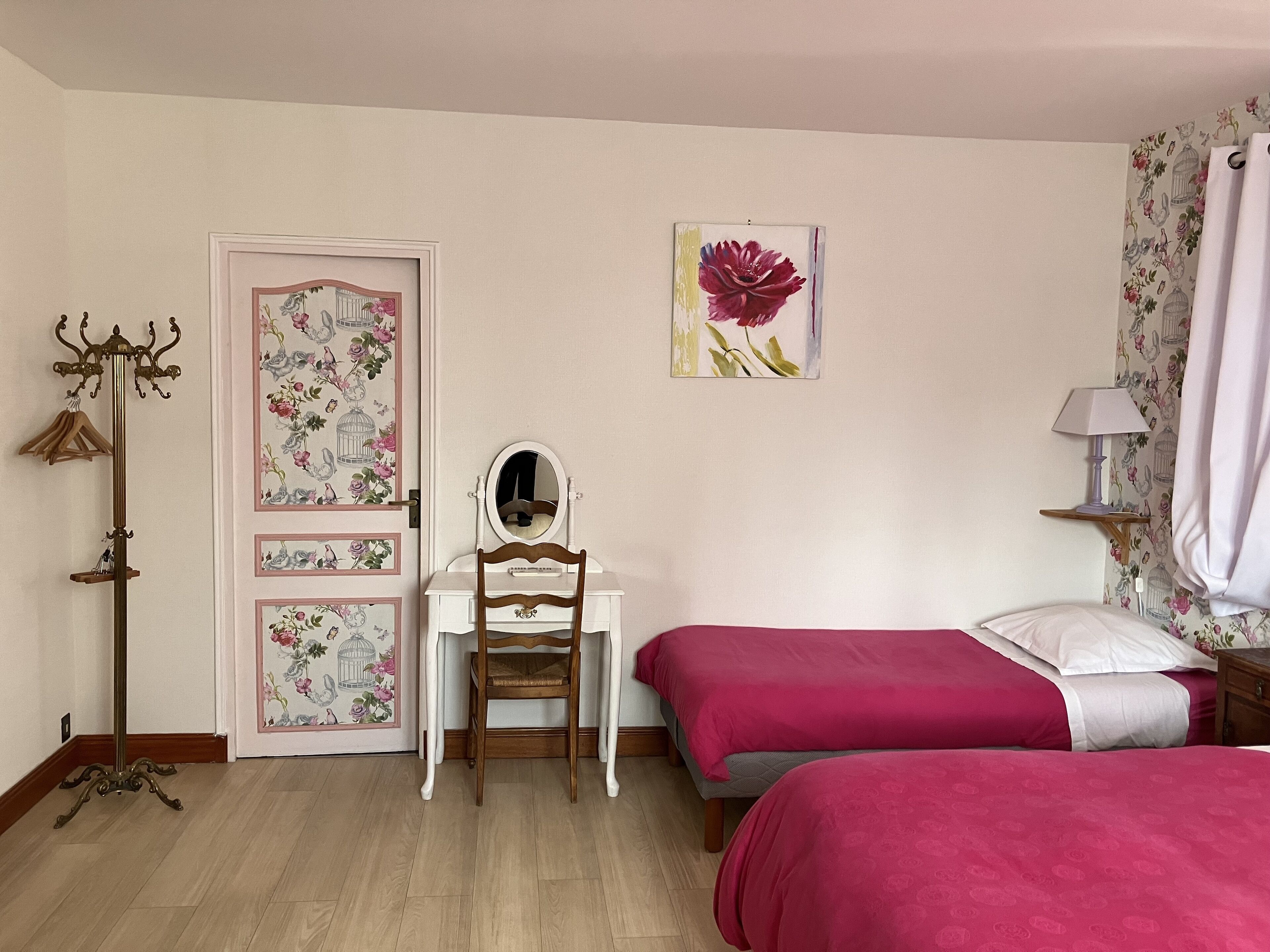 A bedroom with two beds, a dresser, a mirror, a coat rack, and floral wallpaper.