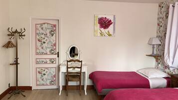 A bedroom with two beds, a dresser, a mirror, a coat rack, and floral wallpaper.