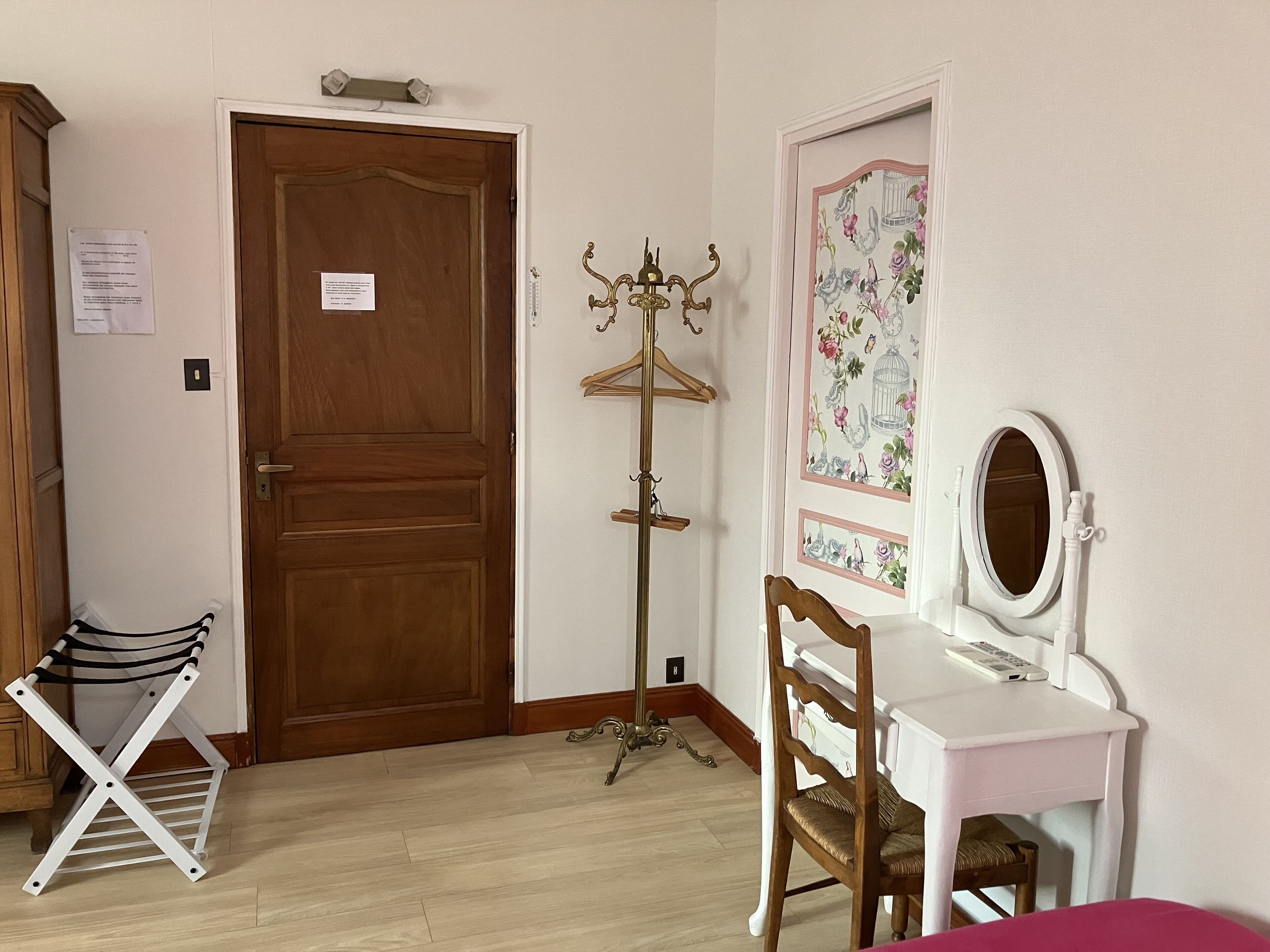Una habitación con puerta de madera, perchero, tendedero, tocador con espejo y un papel tapiz floral en la pared.