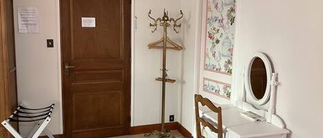 Una habitación con puerta de madera, perchero, tendedero, tocador con espejo y un papel tapiz floral en la pared.