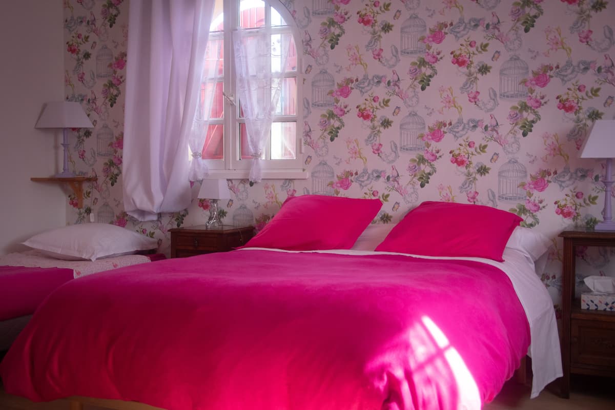 Une chambre à coucher avec un grand lit, un papier peint à motifs floraux et une fenêtre avec des rideaux.