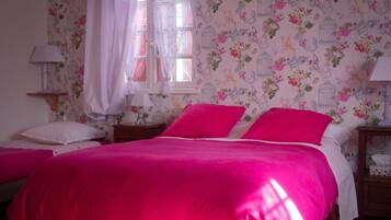 A bedroom with a large bed, floral wallpaper, and a window with curtains.