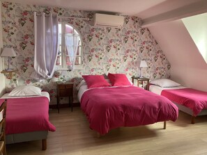 Une chambre avec deux lits, un papier peint à motifs floraux, une fenêtre avec des rideaux et un appareil de climatisation.