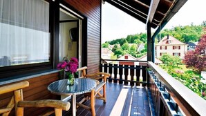 Un balcon avec une balustrade en bois, une table ronde avec des chaises et un vase de fleurs.