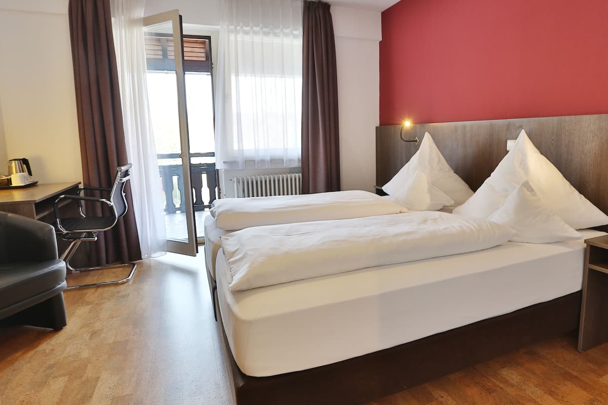 Habitación de hotel con cama, mesitas de noche, una silla y vistas al exterior.
