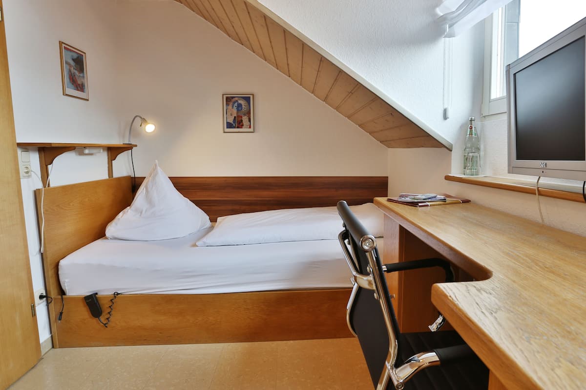 Una habitación pequeña con cama, escritorio y televisión.