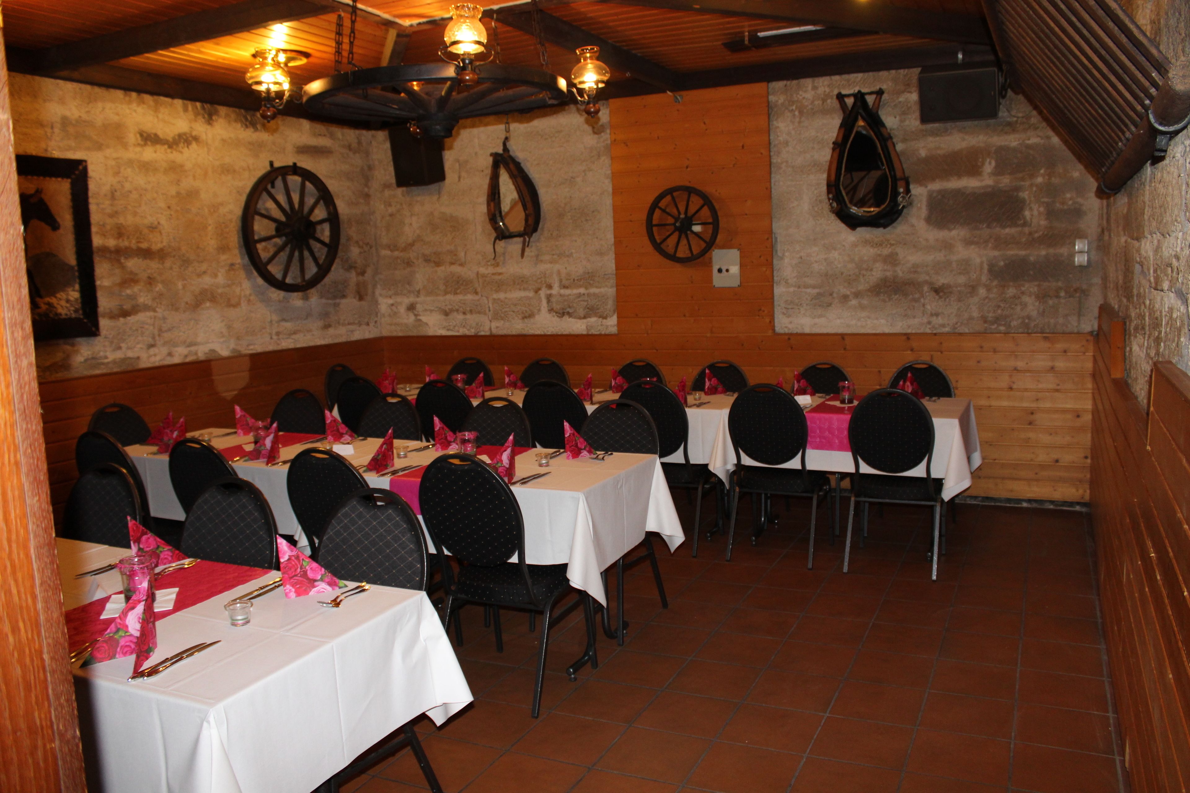 Una sala de banquetes amb diverses taules preparades per dinar, amb una paret de pedra rústica i un sostre de fusta.