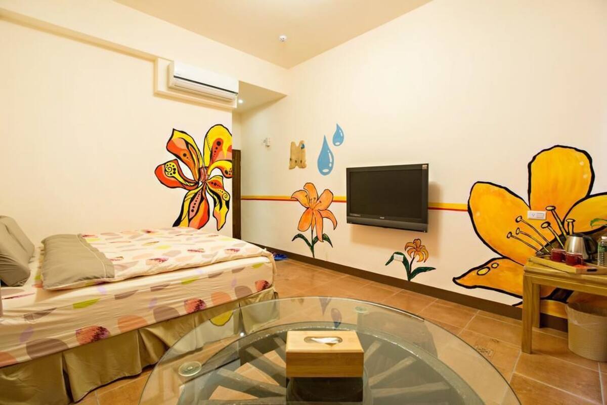 Une chambre à coucher comprenant un lit, une table en verre, un téléviseur et des œuvres d’art murales représentant des fleurs et un papillon.