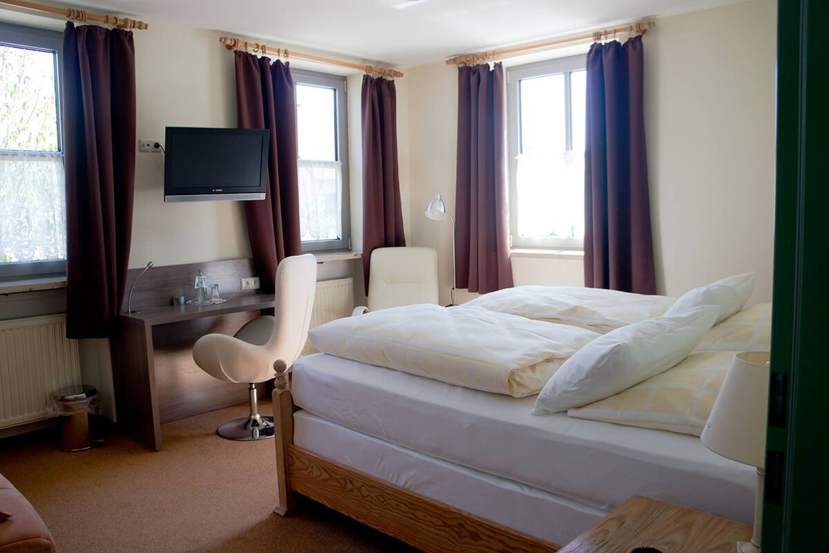 Een hotelkamer met een bed, een bureau met stoel, een televisie en een raam met gordijnen.