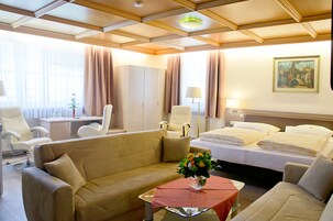 A hotel room with a sofa, a bed, a desk, and a painting on the wall.