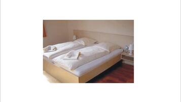A double bed with white linens and pillows, a wooden headboard, and a bedside table with a lamp.