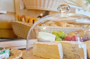 A cheese display with a glass dome, including various types of cheese and some fruits.