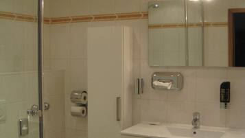 A bathroom with a glass shower enclosure, a toilet, a sink with a mirror, and a towel dispenser.