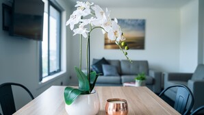 A modern living room with a wooden table, a white vase with white flowers, and a copper candle holder. - Youngtown Executive Apartments (Youngtown)