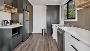 A modern kitchen with dark cabinetry, a stainless steel refrigerator, a built-in oven, and a window providing a view of the outdoors. - Youngtown Executive Apartments (Youngtown)