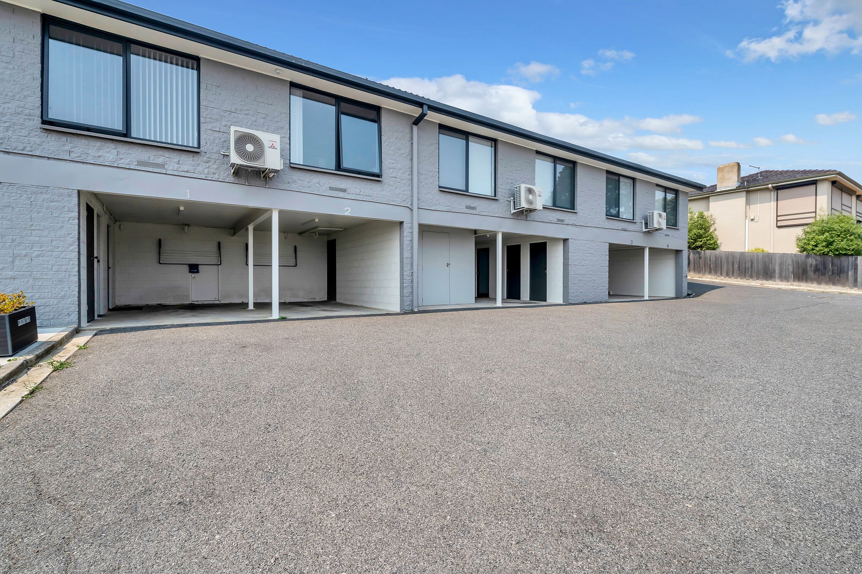 A two-story residential building with multiple garage doors and air conditioning units.