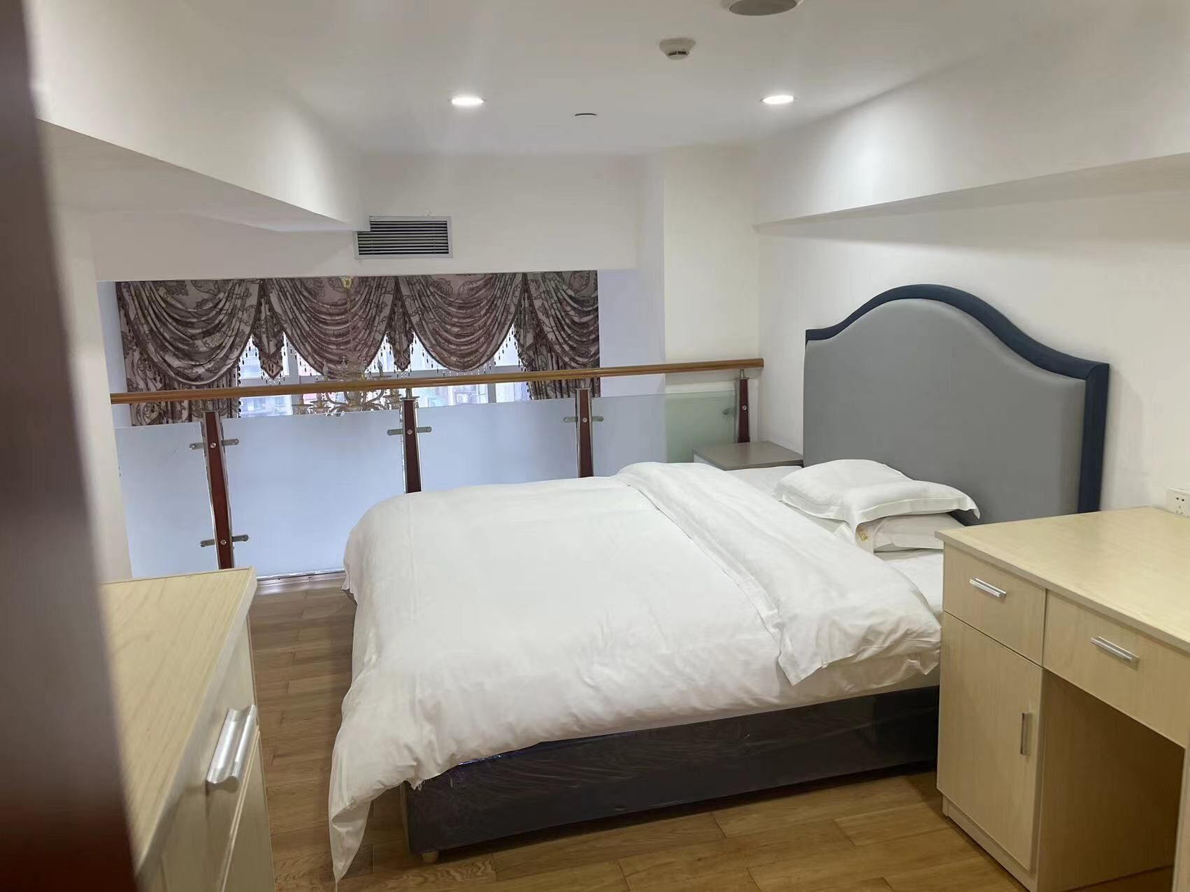 A bedroom with a bed, bedside table, and a view of a balcony with curtains.