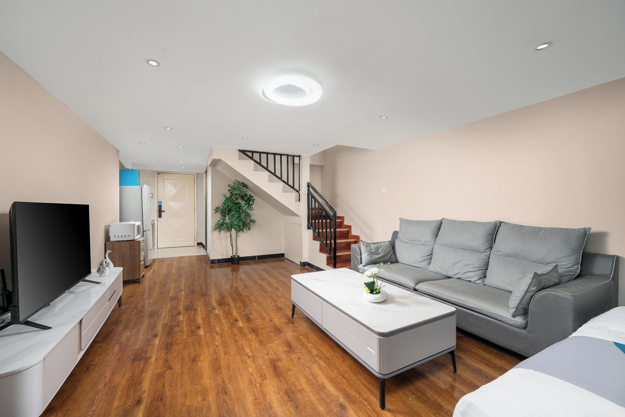 A modern living room with a flat-screen TV, a grey sofa, a white coffee table, and a staircase leading to another level.
