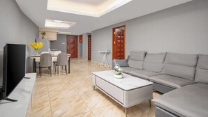 Un salon moderne doté d’un téléviseur à écran plat, d’un canapé gris, d’une table basse blanche et d’un coin repas avec des chaises et une table.