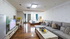 A modern living room with a flat-screen TV, a sofa, a coffee table, and a dining area with a table and chairs. - YOYO International Apartment (Guangzhou)