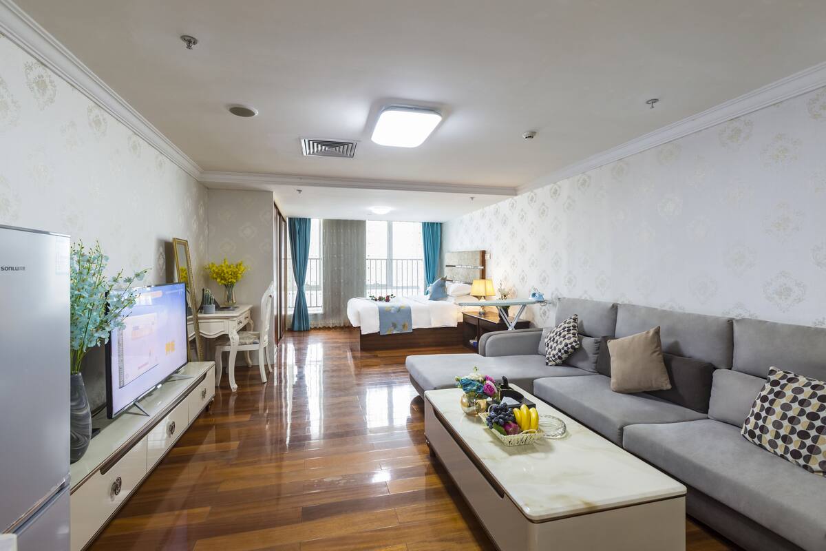 A modern living room with a flat-screen TV, a sofa, a coffee table, and a dining area with a table and chairs.