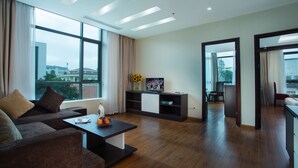 Un salon moderne avec un canapé, une table basse et un meuble pour la télévision. Une grande fenêtre, ornée de rideaux, offre une vue sur les bâtiments environnants.